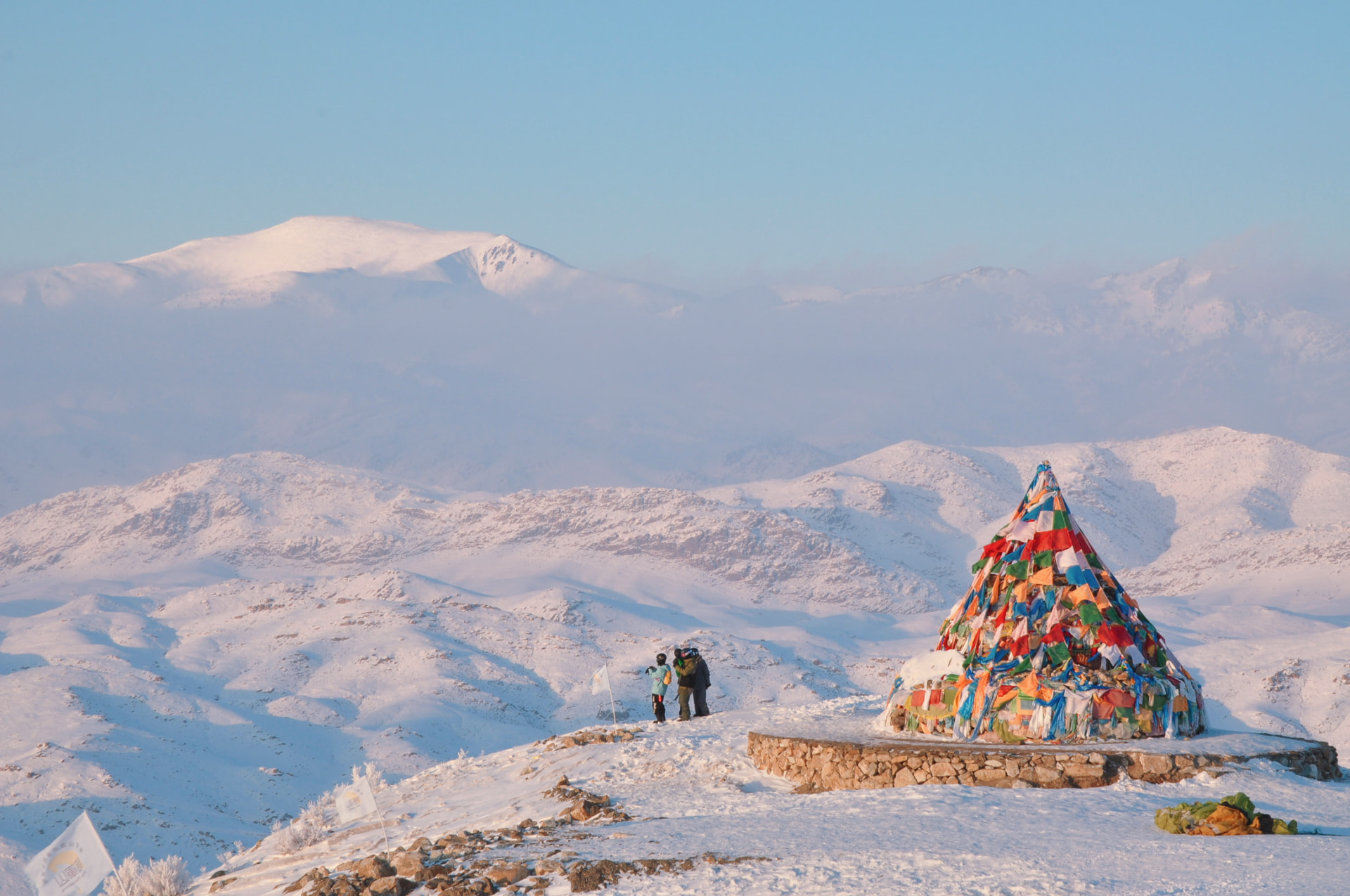 A cone of colourful prayer flags on a snowy plateau above a frozen mountain valley