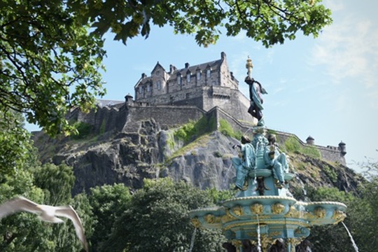 Edinburgh Castle rising above trees, framed by the Ross Fountain in the foreground